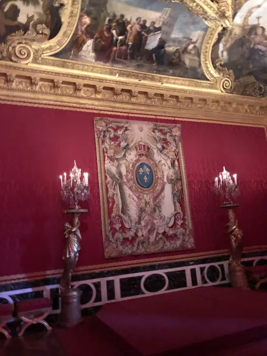 The arms of France, woven and framed against the red of a state salon.